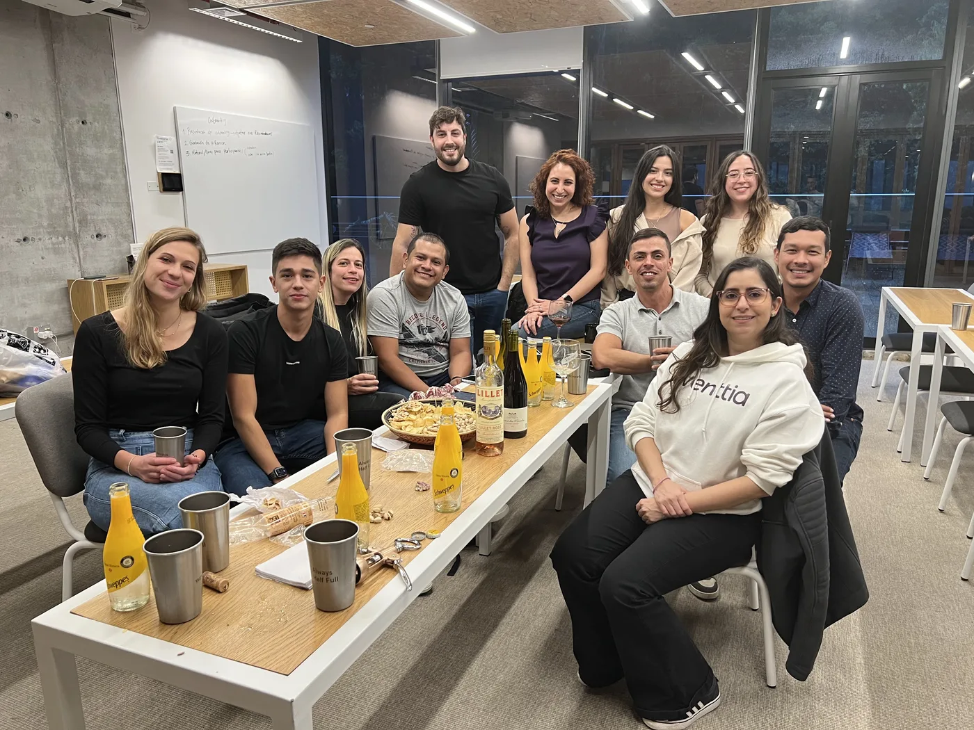 Around eleven Eventtia team members gathered around a long office table in the evening, drinks out, one person in an eventtia-branded hoodie.