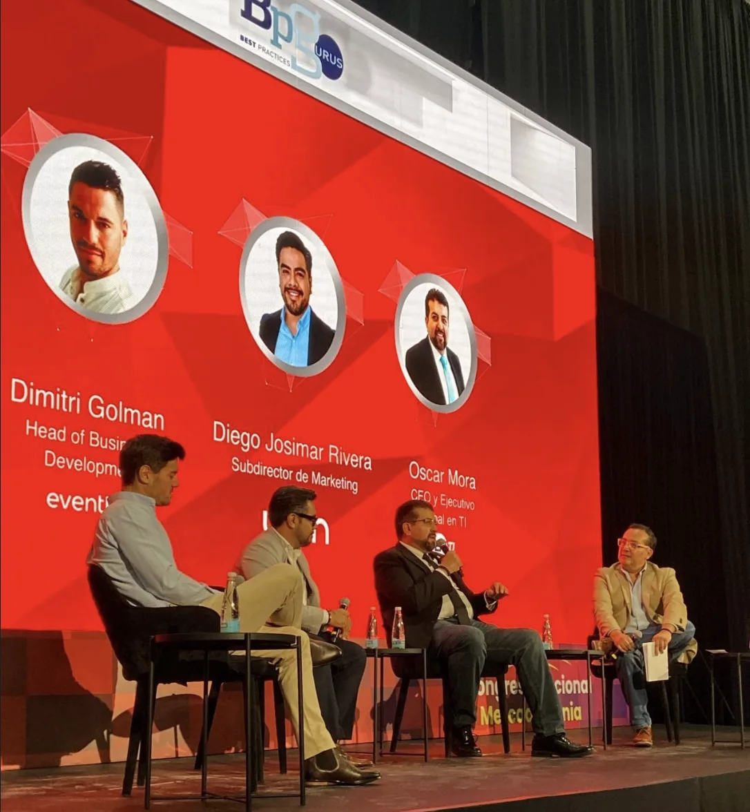 Panel of four speakers on stage at a Merca2.0 event in Mexico City, red backdrop showing speaker portraits including Eventtia's Dimitri Golman.