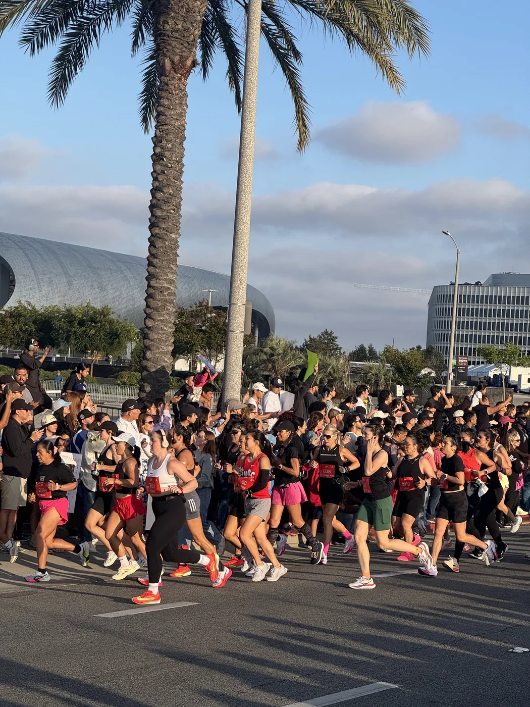 Runners at the start of the Nike After Dark Tour in Los Angeles, palm tree and arena in the background, golden-hour light.