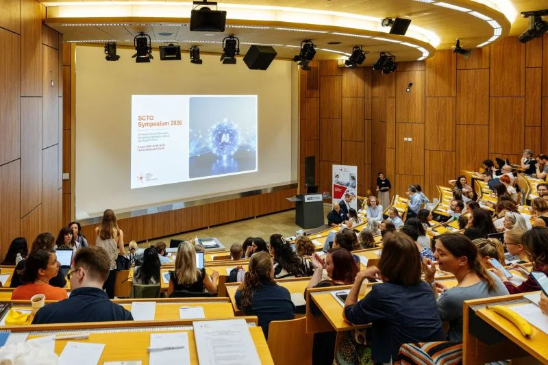 Packed auditorium at the SCTO Symposium 2026, projected slide reading 'SCTO Symposium 2026' at the front.