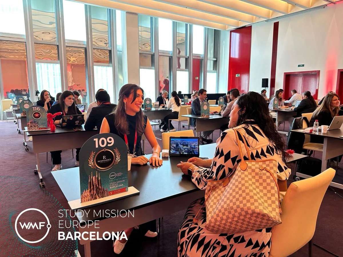 B2B meetings in a sunlit room at WMF Study Mission Europe in Barcelona, attendees seated at numbered tables (table 109 visible), laptops open.